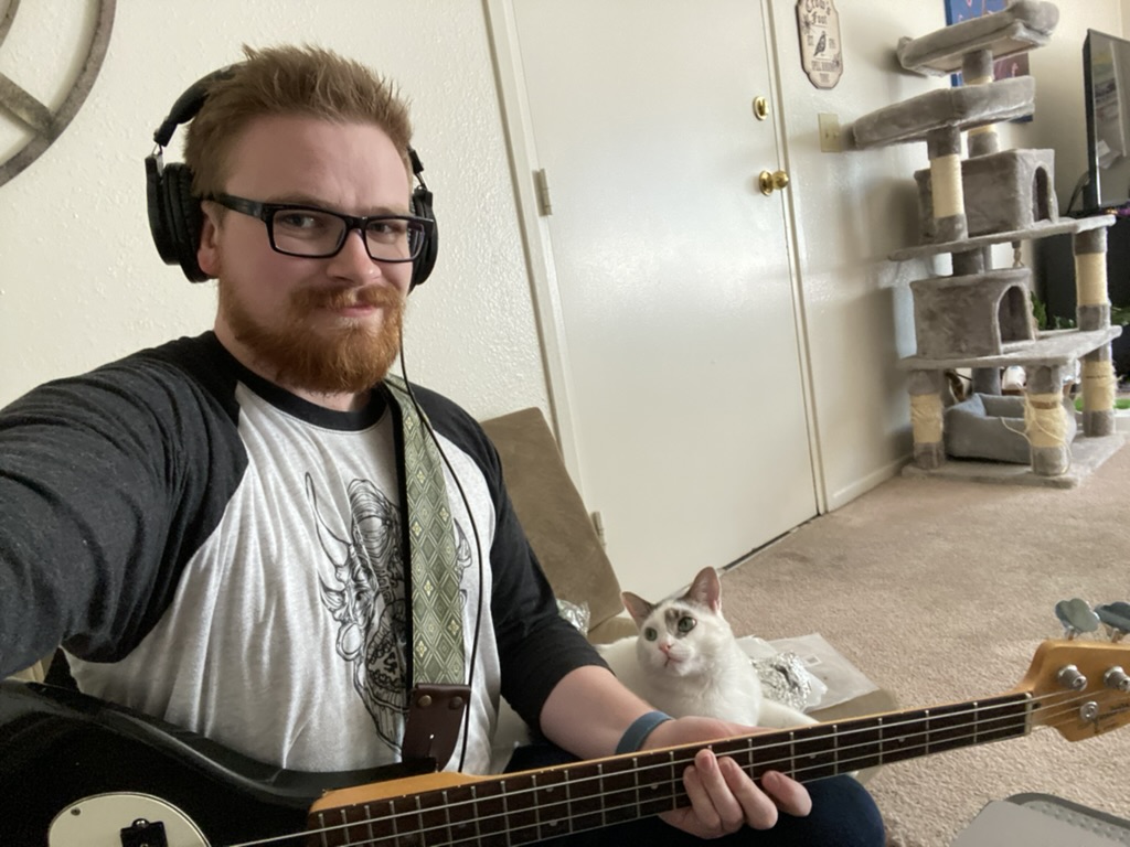 Marshall looking at the camera while 
                    sitting and holding a bass guiatar